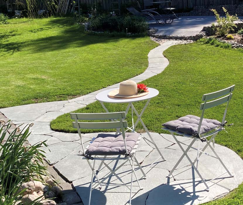 Smal stengång genom gräset upp till en liten stenbelagd uteplats.