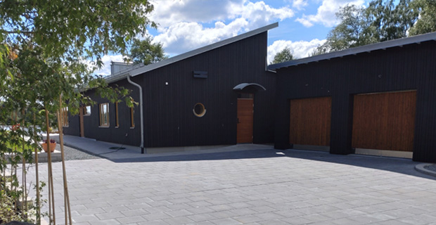 Stor stenbelagd uppfart mot ett svart hus med ett dubbelgarage.